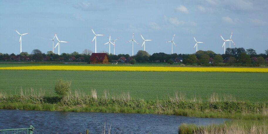 Landschaft mit Feldern, im Hintergrund sind Windräder zu sehen